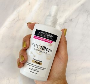 Hand with gold painted fingernails holding a bottle of thickening spray